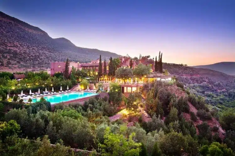 A charming hotel enveloped by verdant trees and towering mountains, offering a peaceful retreat in nature's embrace.